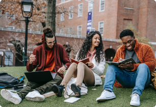 A group of students sitting on the grass looking at a laptop and reading.